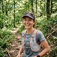 Realistic close-up portrait of a 34-year-old French woman trail runner, outdoor in a forest trail, smiling, wearing trail running gear (hydration vest, cap, sunglasses on head), natural lighting, medium shot, high resolution, candid happy expression, blurred green forest background.